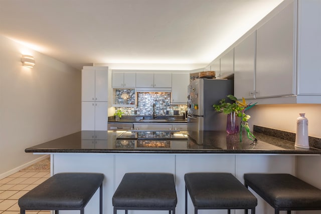kitchen featuring a peninsula, a breakfast bar, freestanding refrigerator, a sink, and baseboards