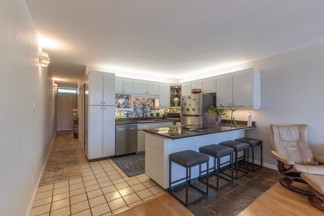 kitchen featuring baseboards, a kitchen bar, a peninsula, dark countertops, and stainless steel appliances