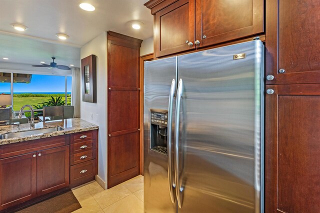 kitchen featuring light stone countertops, light tile patterned floors, stainless steel fridge, a ceiling fan, and a sink