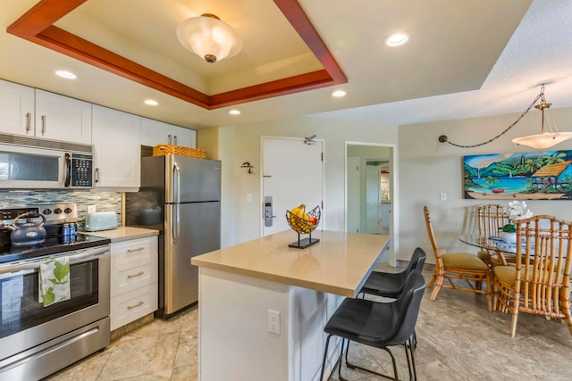 kitchen featuring a breakfast bar, white cabinetry, appliances with stainless steel finishes, a raised ceiling, and decorative backsplash