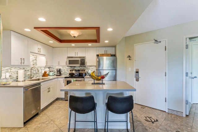 kitchen featuring sink, appliances with stainless steel finishes, a kitchen breakfast bar, a tray ceiling, and white cabinets