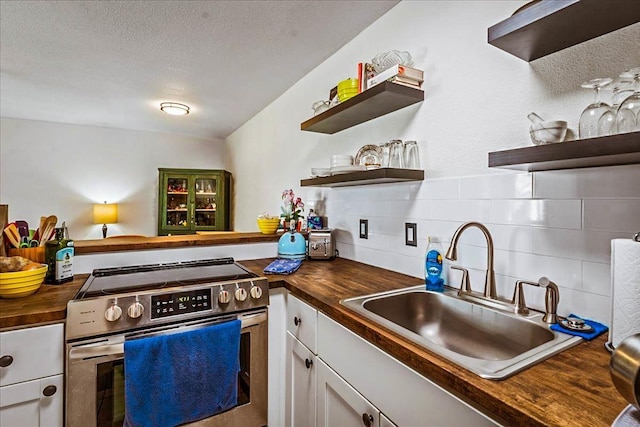 kitchen featuring butcher block countertops, white cabinets, sink, and stainless steel range