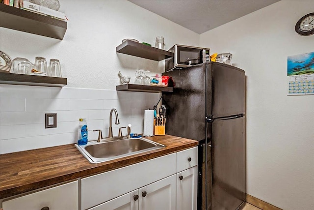 kitchen featuring wood counters, tasteful backsplash, black fridge, sink, and white cabinets