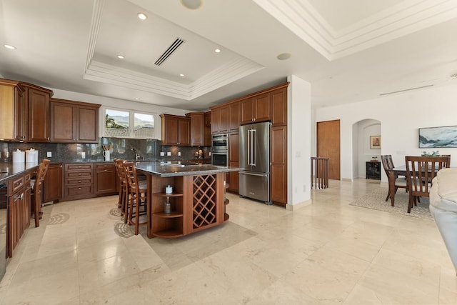 kitchen with a raised ceiling, backsplash, a center island, and appliances with stainless steel finishes