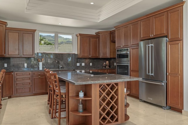 kitchen with a center island, a raised ceiling, a breakfast bar area, decorative backsplash, and stainless steel appliances