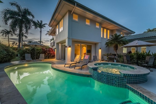 back house at dusk with a patio area and a swimming pool with hot tub