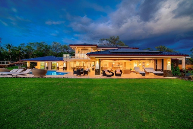 back house at dusk featuring an outdoor living space, a patio area, a yard, and a balcony