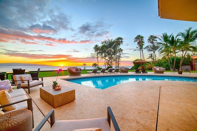 pool at dusk featuring an outdoor hangout area, a water view, and a patio