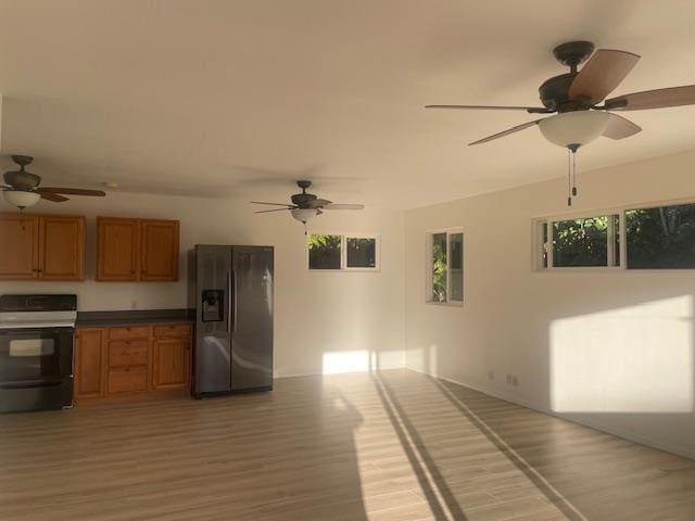 kitchen featuring dark countertops, light wood-style floors, brown cabinetry, range with electric cooktop, and stainless steel fridge