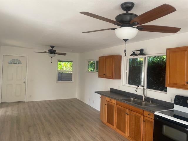 kitchen with brown cabinetry, dark countertops, black range with electric cooktop, and a sink