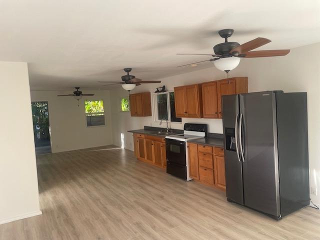 kitchen featuring stainless steel fridge, brown cabinetry, dark countertops, light wood-type flooring, and range with electric stovetop