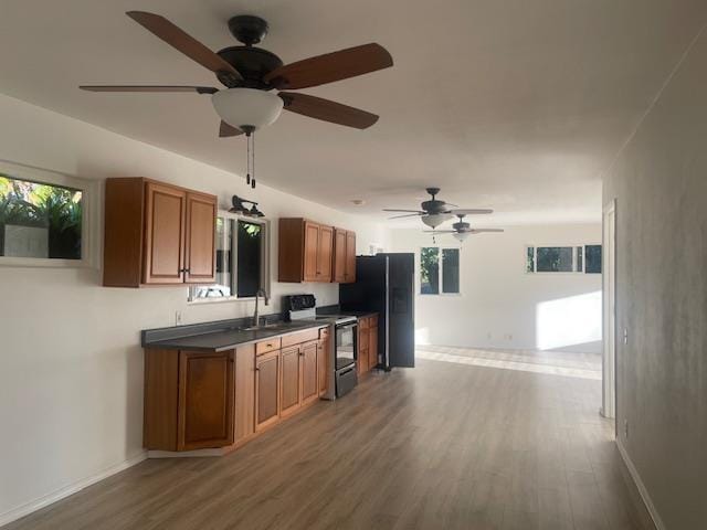 kitchen featuring electric range, a sink, freestanding refrigerator, brown cabinetry, and dark countertops