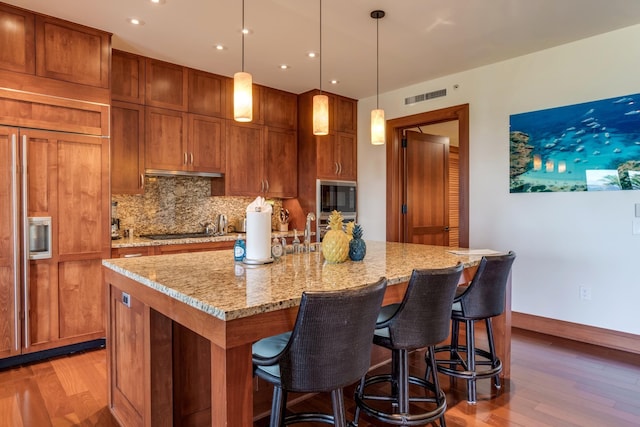 kitchen featuring backsplash, wood finished floors, visible vents, and built in appliances