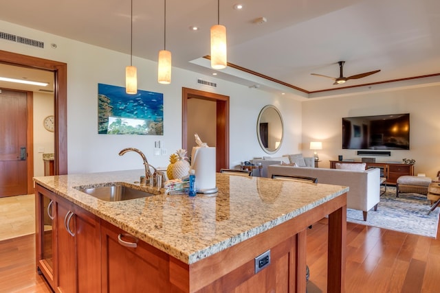 kitchen featuring light wood finished floors, visible vents, light stone countertops, brown cabinets, and a sink