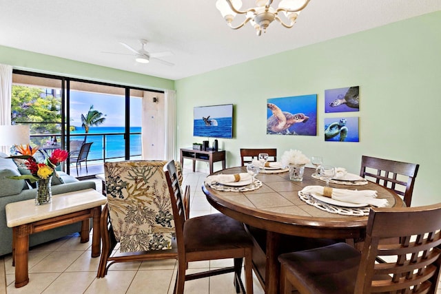 dining room with ceiling fan with notable chandelier, light tile patterned flooring, and a water view