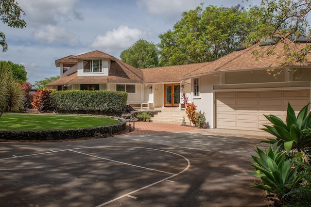 view of front of house with a garage, a front lawn, roof with shingles, stucco siding, and french doors