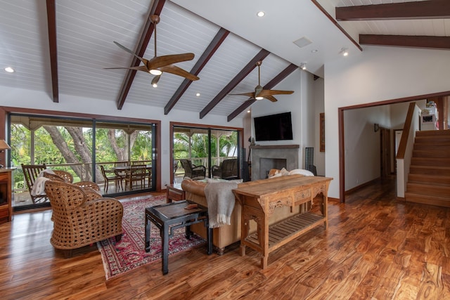 living room with wood finished floors, a fireplace, beamed ceiling, baseboards, and ceiling fan
