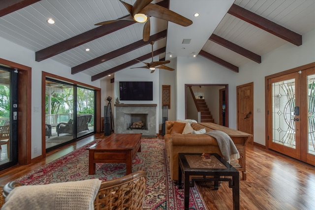 living area featuring french doors, a ceiling fan, vaulted ceiling with beams, light wood-type flooring, and stairway
