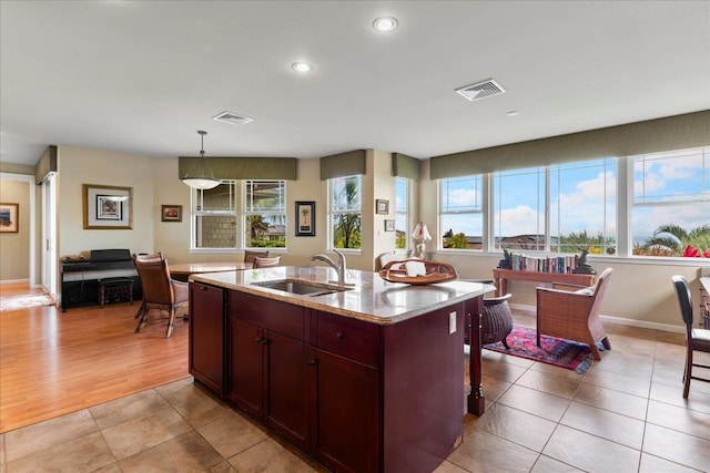 kitchen with a sink, light stone counters, a kitchen island with sink, and visible vents