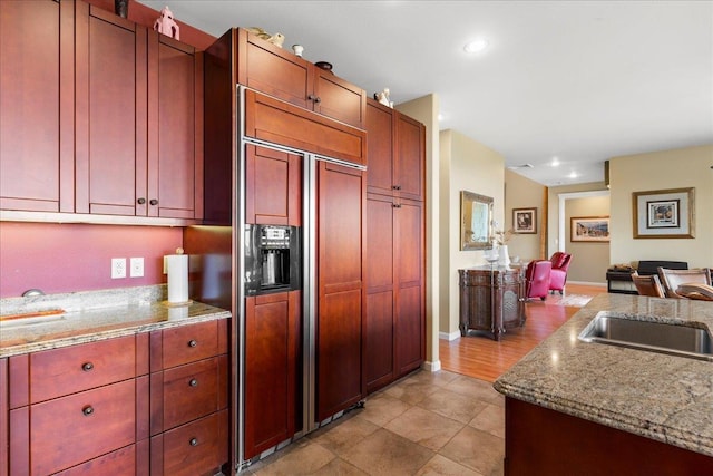kitchen featuring reddish brown cabinets, light stone countertops, a sink, paneled built in refrigerator, and open floor plan