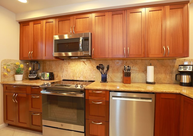 kitchen with stainless steel appliances, tasteful backsplash, brown cabinets, and light stone countertops