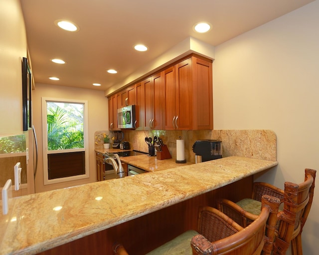 kitchen featuring light stone counters, stainless steel microwave, backsplash, and a breakfast bar