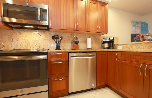 kitchen featuring brown cabinets, light tile patterned floors, stainless steel appliances, tasteful backsplash, and light stone countertops