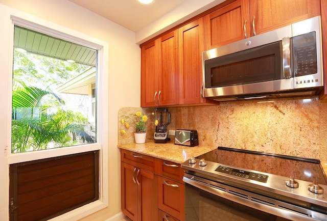 kitchen with appliances with stainless steel finishes, brown cabinetry, light stone counters, and tasteful backsplash