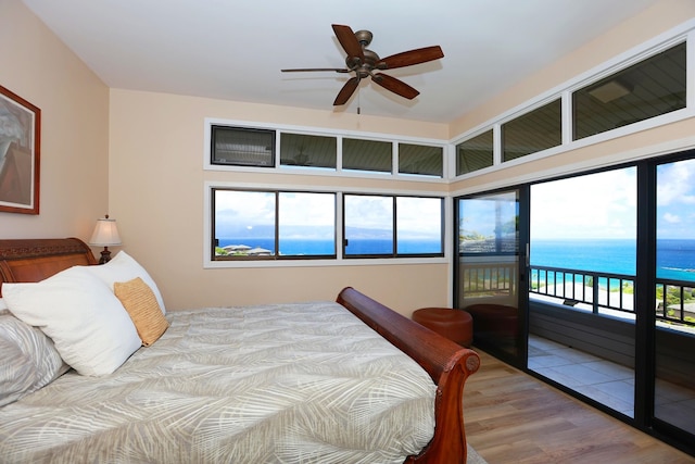 bedroom featuring access to outside, a water view, multiple windows, and wood finished floors