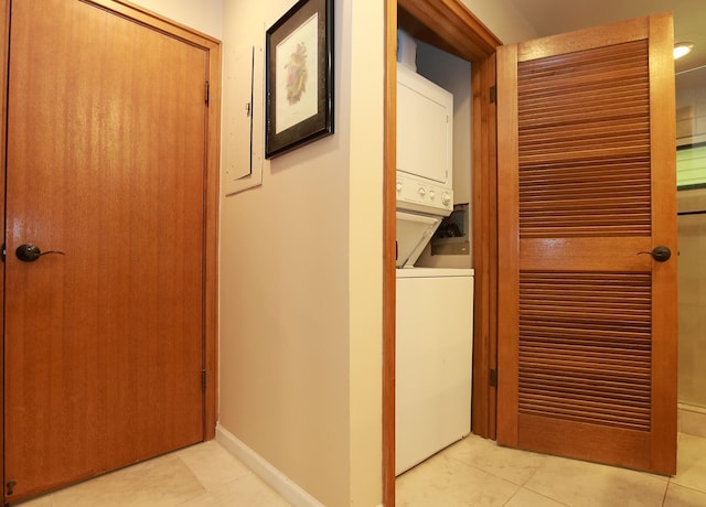 laundry area featuring laundry area, light tile patterned floors, baseboards, and stacked washer and clothes dryer