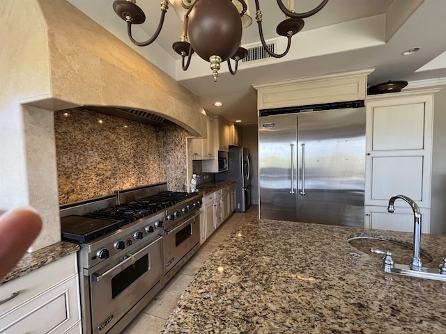 kitchen with custom range hood, backsplash, dark stone counters, light tile patterned floors, and high end appliances