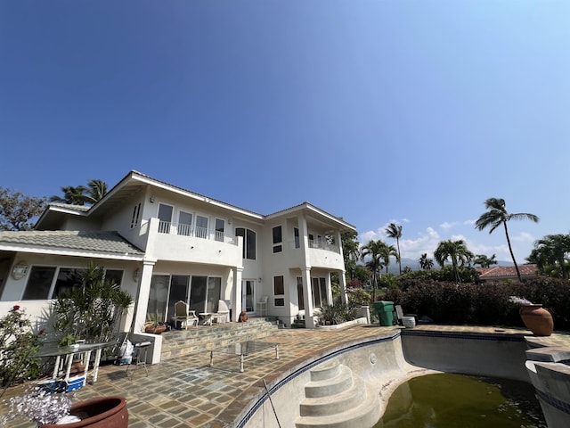 rear view of property with stucco siding, a patio, a balcony, and a fenced in pool