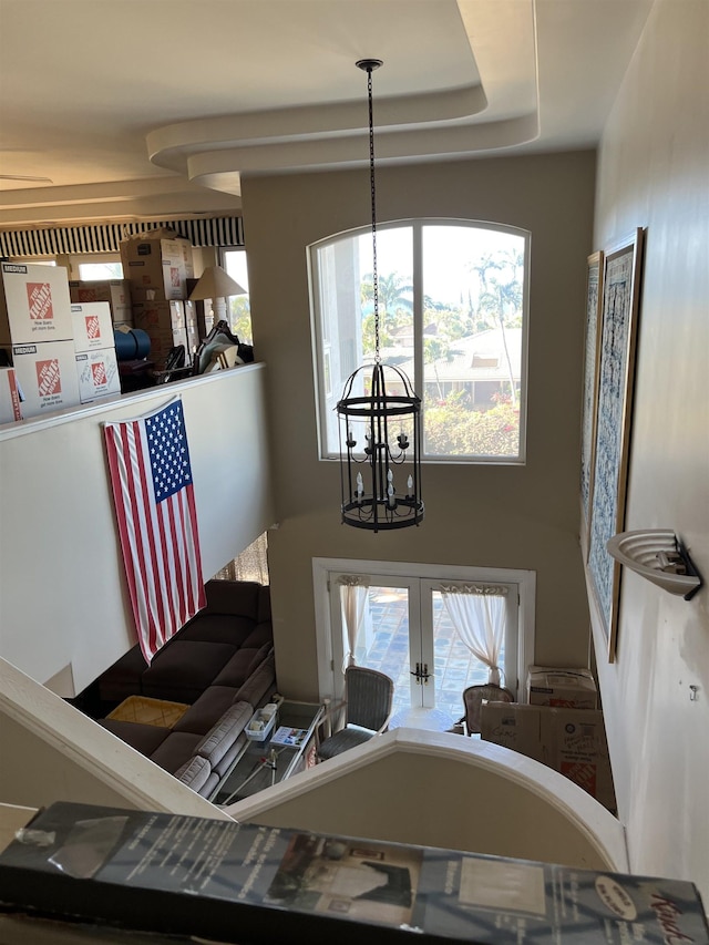 interior space with an inviting chandelier, a raised ceiling, and french doors