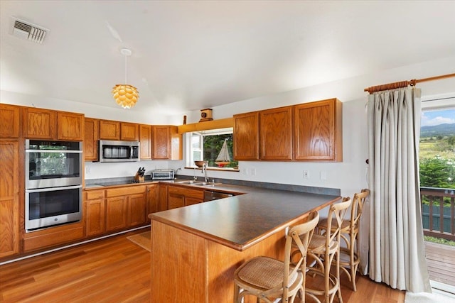 kitchen featuring kitchen peninsula, appliances with stainless steel finishes, light wood-type flooring, and decorative light fixtures