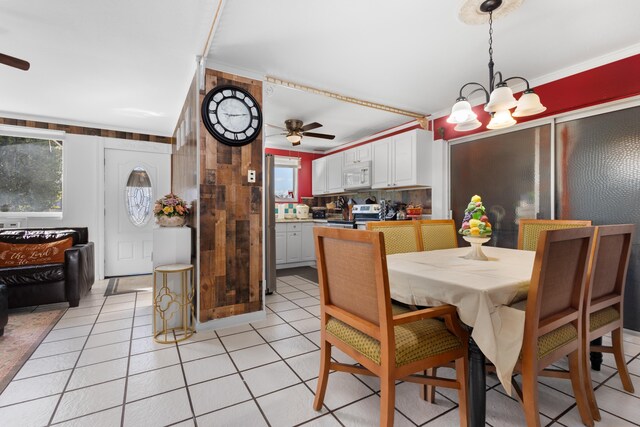 dining area with ceiling fan with notable chandelier, light tile patterned floors, and crown molding