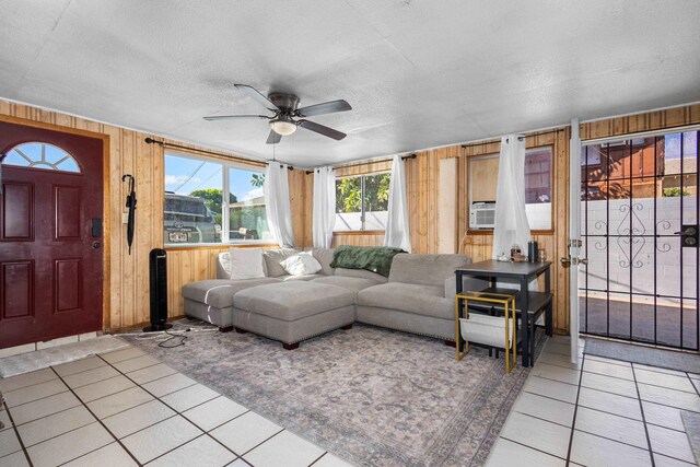 living room featuring light tile patterned floors, a textured ceiling, ceiling fan, and wood walls