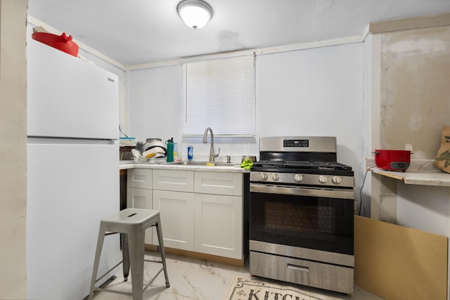 kitchen with stainless steel gas stove, white fridge, white cabinetry, and sink