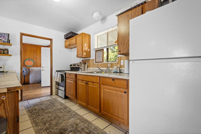 kitchen with light tile patterned flooring, sink, white fridge, and stainless steel stove