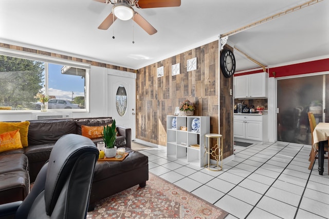 living room featuring ornamental molding, ceiling fan, wooden walls, and light tile patterned flooring