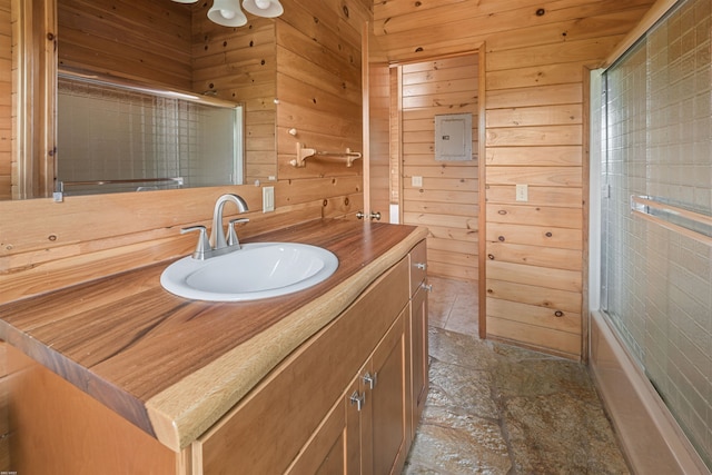 bathroom featuring enclosed tub / shower combo, vanity, and wood walls