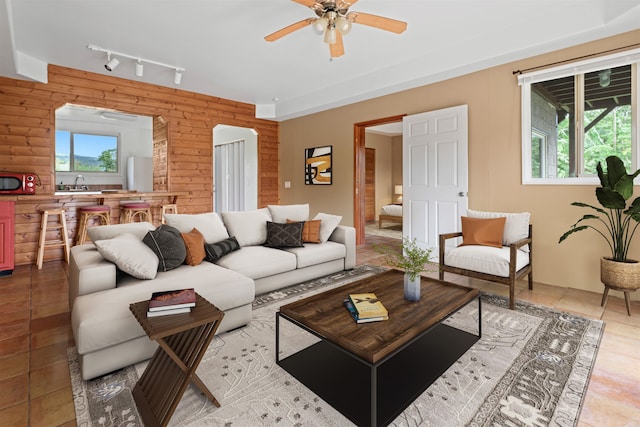 living room featuring sink, rail lighting, wooden walls, light tile patterned floors, and ceiling fan