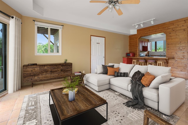 living room with wooden walls, ceiling fan, light tile patterned floors, and rail lighting