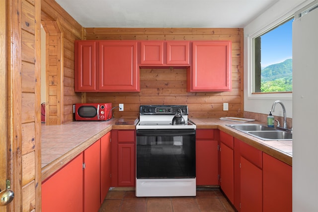 kitchen with tile counters, wooden walls, sink, and electric range