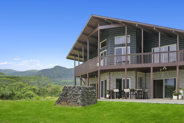 back of property with a lawn, a mountain view, a balcony, and a patio area