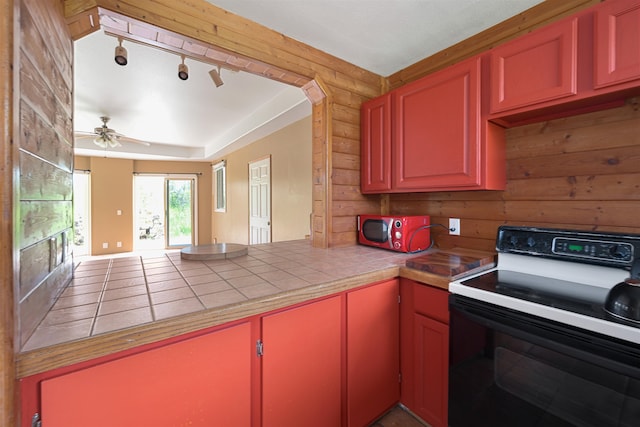 kitchen with tile counters, wooden walls, electric stove, and ceiling fan