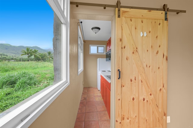 corridor with tile patterned flooring, a mountain view, a healthy amount of sunlight, and a barn door