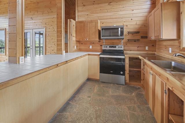 kitchen featuring sink, stainless steel appliances, wooden walls, tile countertops, and french doors