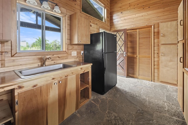 kitchen featuring sink, lofted ceiling, wooden walls, black refrigerator, and wooden ceiling