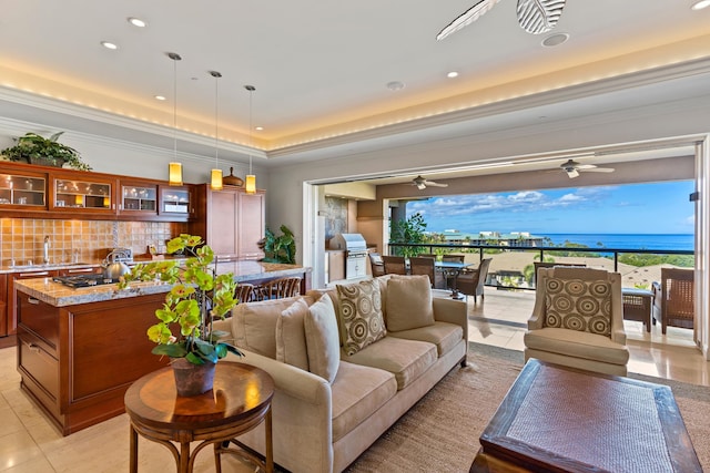 tiled living room featuring ceiling fan, a water view, a raised ceiling, and plenty of natural light