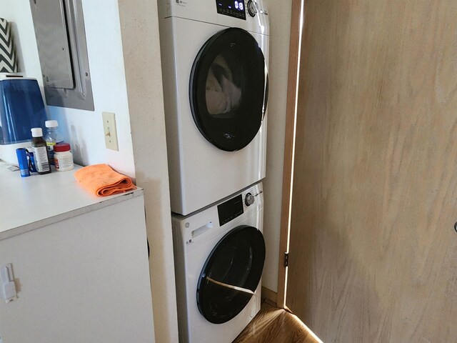 laundry area with electric panel, wood-type flooring, and stacked washer and dryer